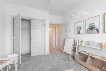 A room with a white door, a white table, a white chair, a white shelf, and three framed pictures on the wall.